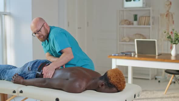 A Physical Therapist Is Giving Massage Therapy To a Black Man Who Is Lying on a Couch alt