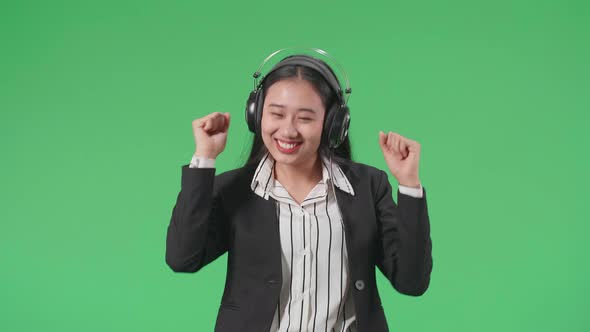 An Asian Business Woman Listening To Music With Headphones And Dancing In The Green Screen Studio alt