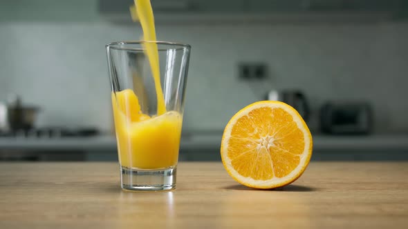 Filling glass with orange juice in the kitchen on wooden table with half of orange fruit. Close up