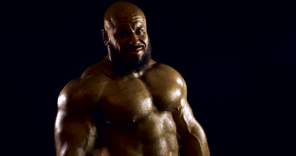 Naked Bodybuilder Man Is Standing in Darkness in Studio, Showing Muscles of Torso alt