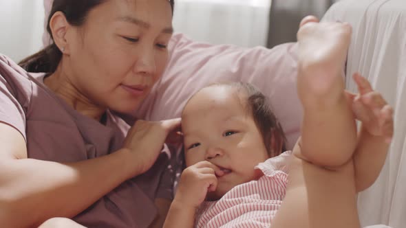 Happy Asian Mom Bonding with Sweet Toddler Girl on Sofa alt