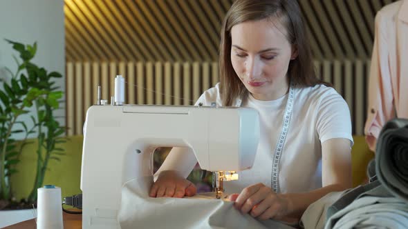 Young Woman Seamstress Sews on a Sewing Machine Sitting at a Table alt