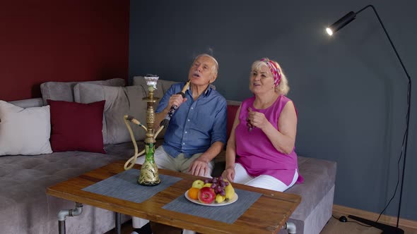 Elderly Couple Smoking Hookah at Home. Senior Grandmother and Grandfather Having Fun, Relaxing alt
