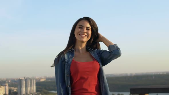 Beautiful Brunette Girl Smiling, Touching Hair on Cityscape Background Slow-Mo