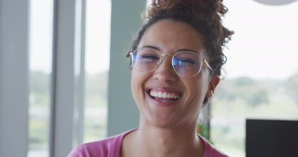 Portrait of smiling biracial creative businesswoman wearing glasses in modern office interior alt