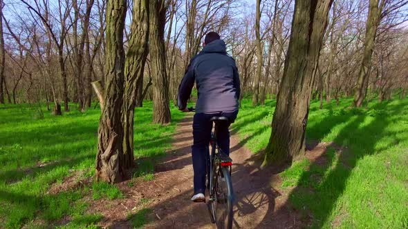 Young Guy Rides a Bicycle Along a Path in a Green Forest Rear View in Slow Mo alt