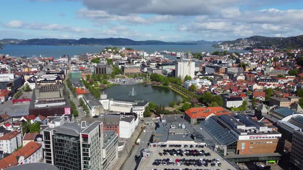 Forwarding aerial Bergen city centre with water fountain in park and seafront in the background - No alt