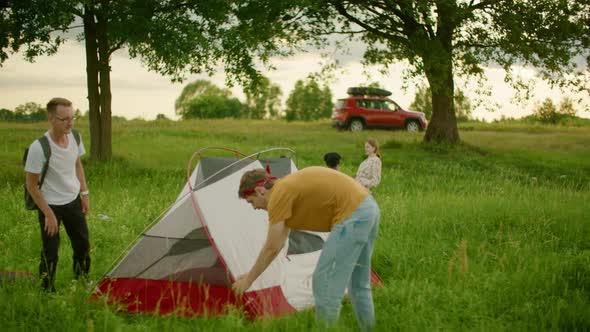 Group of Young Friends Pitch Tent and Prepare Picnic Place on Camping Site