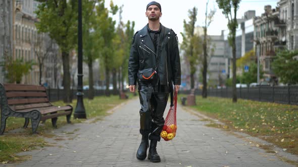 Wide Shot Portrait of Young Confident Gay Man Walking with Shopping Net in Urban City Looking Around alt