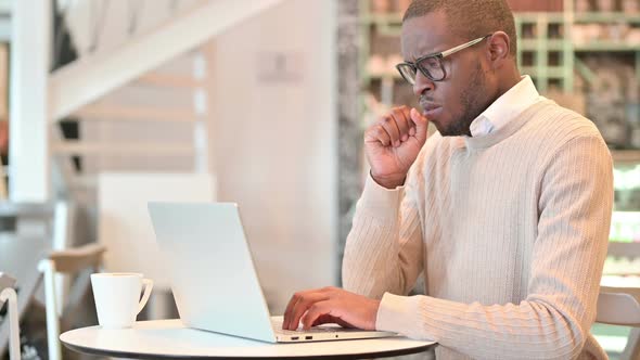 Sick African Man with Laptop Coughing in Cafe alt