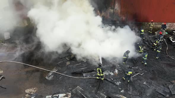 Aerial view of firefighters extinguishing fire in industrial area. alt