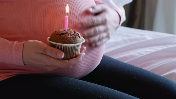 A pregnant woman holds a birthday cake with a candle.