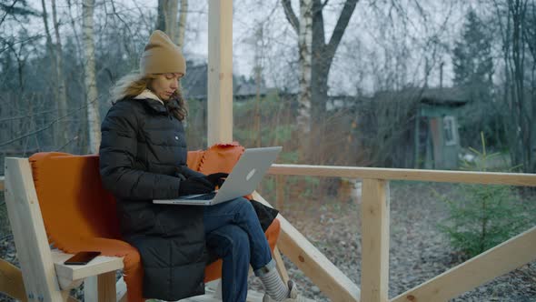Woman in a Down Jacket Winter Hat and Gloves Works on a Laptop