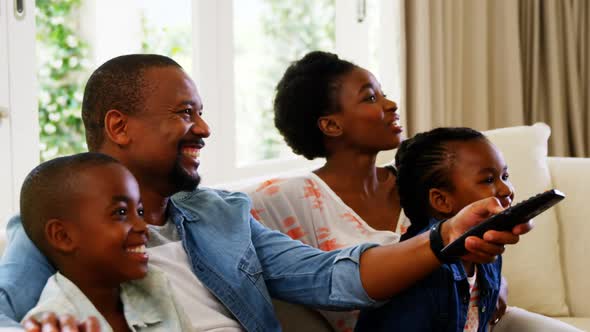 Parents and kids having fun while watching television in living room alt