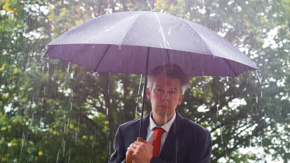 Businessman Sheltering Underneath an Umbrella in the Rain