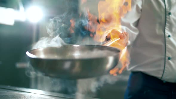 Chef cook cultivates burning alcohol in a frying pan with a lighter for cooking alt