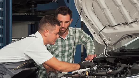 Car Service Mechanic Repairing Automobile While Talking To the Customer alt