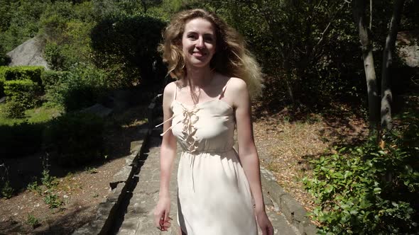 Bright Young Girl Cheerfully Walks Along the Path Among the Beautiful Garden alt