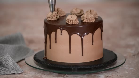 Female hands decorate a sponge cake with chocolate cream from a pastry bag.