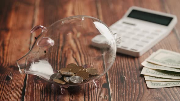 A Hand Inserting Coins in Piggybank Over Wooden Desk alt