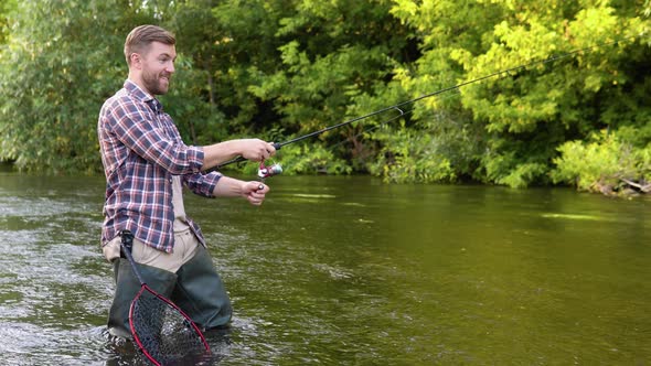 A Fisherman Throws a Fishing Rod Standing Kneedeep in the Water of the River alt