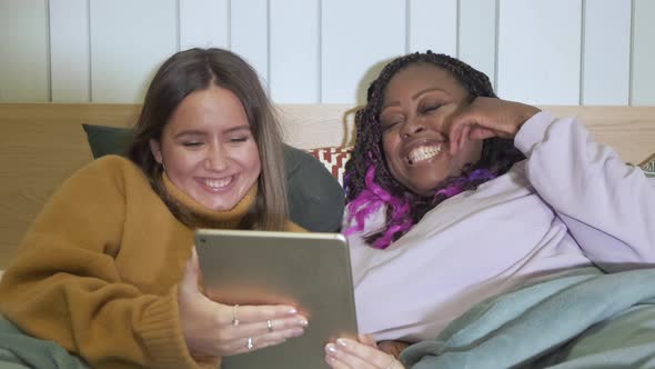 Close - Up Of Girlfriends Lying In Bed Using A Tablet Are At Home, Evening, Smiling, Cozy Apartment alt