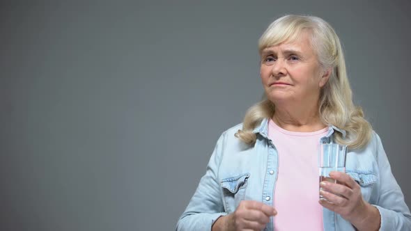 Senior Female Taking Bitter Pill and Wrinkling With Disgust, Heart Medication alt