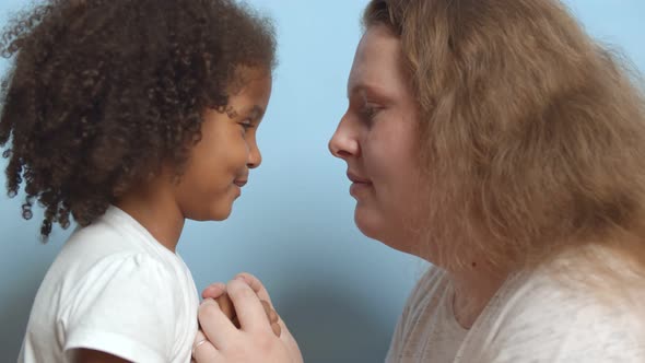 Side View of Caucasian Mother and Mixed Race Daughter Looking at Each Other Isolated Over Blue alt