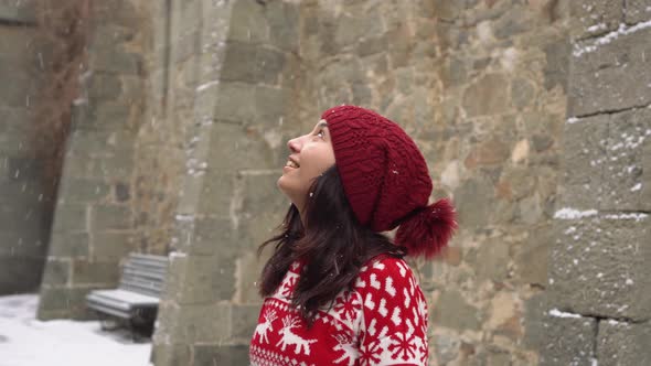 A Happy Female Traveler Looking at the Stone Walls of a Medieval Castle During a Snowfall alt
