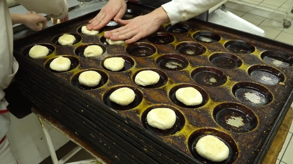 Bakers lay out the dough buns on a baking tray alt