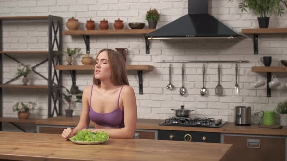 Woman sitting at table, looking sad and bored with diet not wanting to eat salad. alt