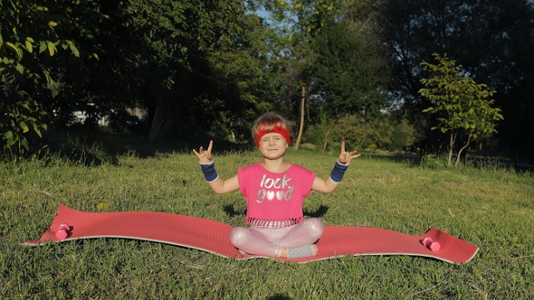 Child Sitting on Mat and Performing Yoga Meditation Outdoors in Park. Girl Doing Yoga Exercises alt