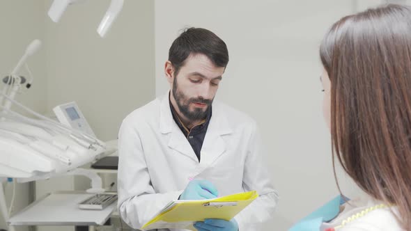 Bearded Dentist Filling Medical Documents While Talking to Patient alt