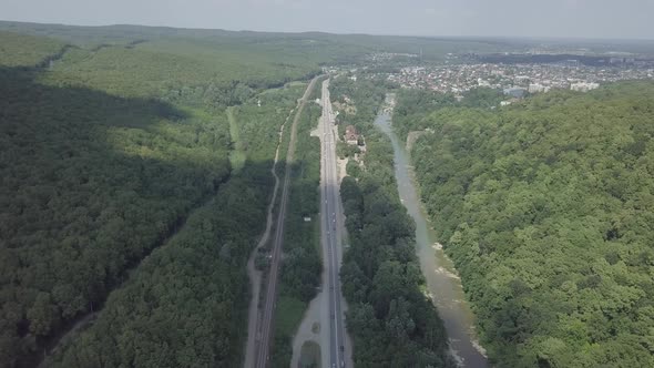 Aerial view of cars driving on asphalt road between green trees in mountain woods along the river