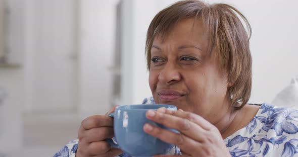 Happy african american senior woman enjoying drinking cup of tea, looking away smiling alt