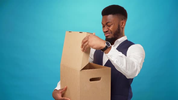 Young African Man Opens Carton Box Dislike What's in It Against Blue Background alt