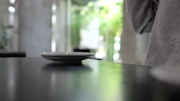 Closeup of a woman drinking and putting a cup of hot coffee down on a saucer