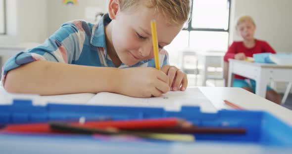 Video of happy caucasian boy sitting at school desk and writing alt