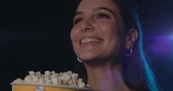 Smiling woman watching a comedy movie and eating popcorn at the cinema