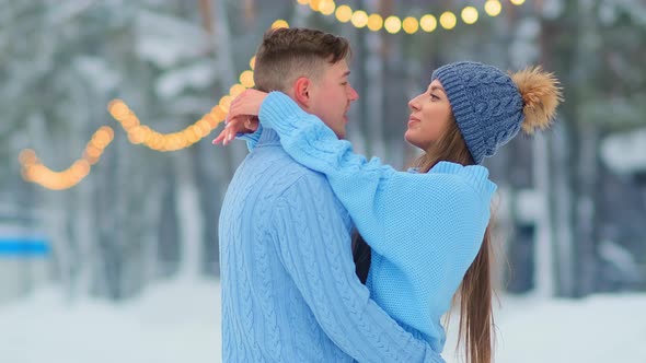 Young Man Hugs Girlfriend in Blue Sweater on Open Ice Rink
