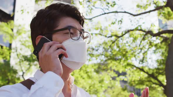 Asian man wearing face mask talking on smartphone on the street alt
