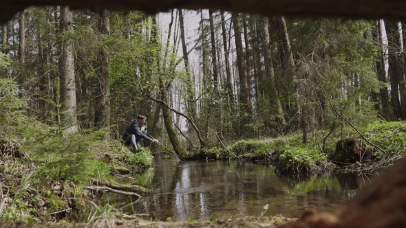 Man Sits Alone on River Bank Pulls Out Tree Branch with Twig Cleans Pond alt