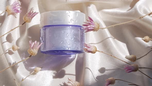 Blue glass cream jar mockup on smooth silk fabric sunlight flowers shadow water splashes Skincare 4K alt