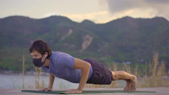 A Young Man Wearing a Protective Face Mask Does Physical Training on a River or Seaside. Physical alt