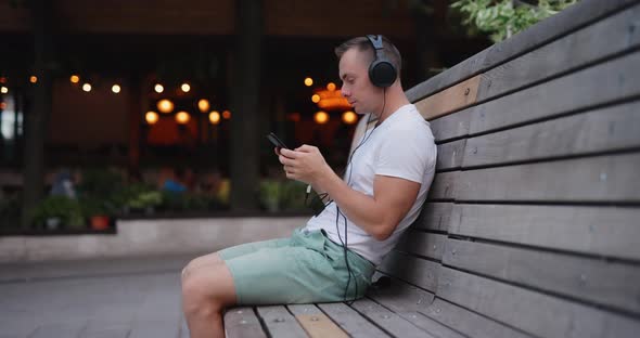 Man Listening to Music in Headphones Sitting on Bench alt
