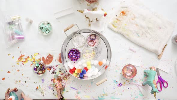 Step by step. Little girls decorating paper mache unicorn with glitter and paper flowers. alt