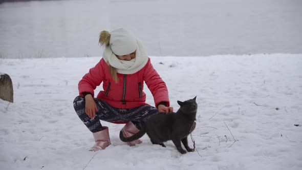 A Young Girl Walks Her Cat in the Snow in Winter