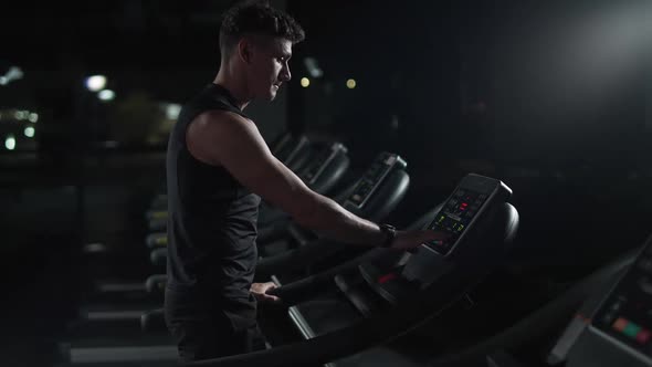 Cinematic Lighting Athletic Man Starts Jogging Run on a Treadmill Aerobic Exercise and Endurance alt