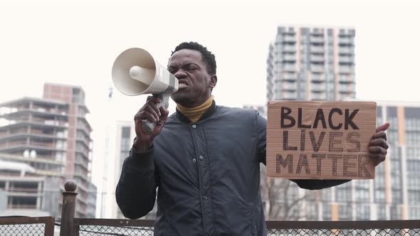 Young Black Man Shouts Angrily with Megaphone and Holds a Sign Black Lives Matter alt
