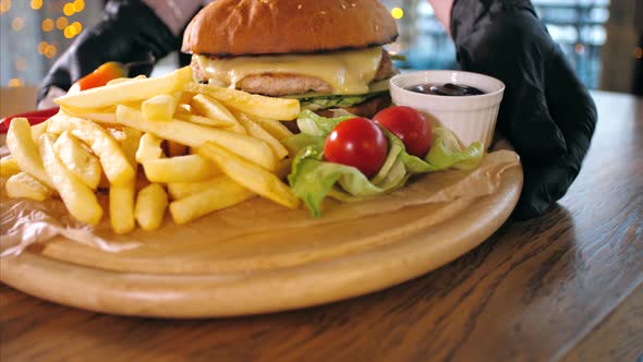 Waiter Put on the Table a French Fries with Burger on Wooden Board